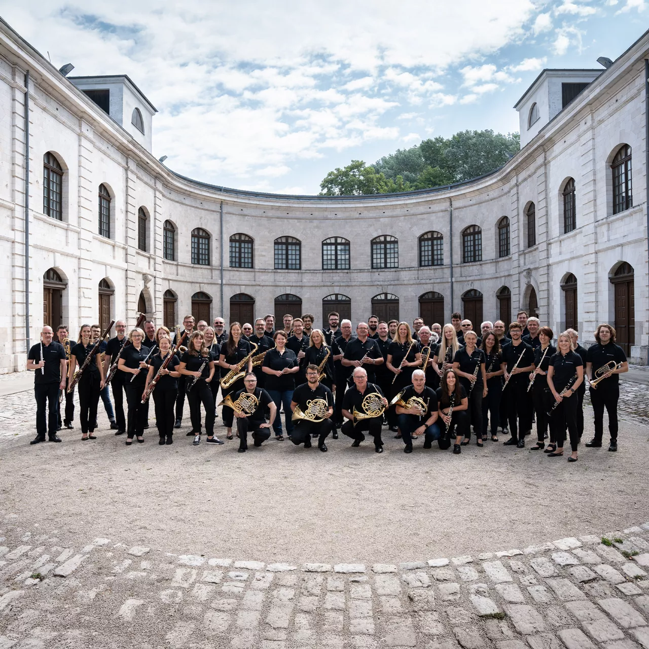 Gruppenfoto der Audi Bläserphilharmonie in schwarzer Kleidung in einem hellen, historischen Innenhof.