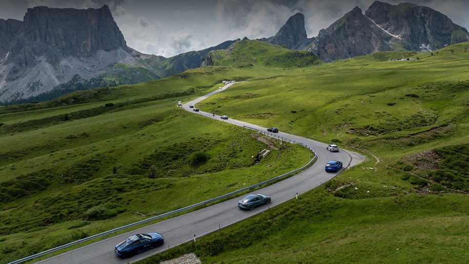 Bird's eye view of a landscape with a winding road on which several Audi models are driving one behind the other, with mountains in the background