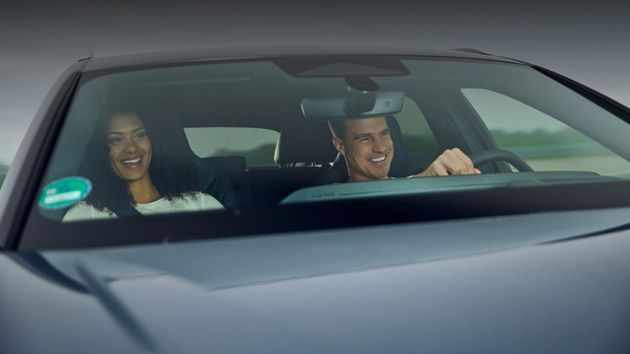 Mann und Frau sitzen in einem Audi Modell, der Mann sitzt am Steuer, beide lächeln. Mehr erfahren Audi driving experience Gutschein