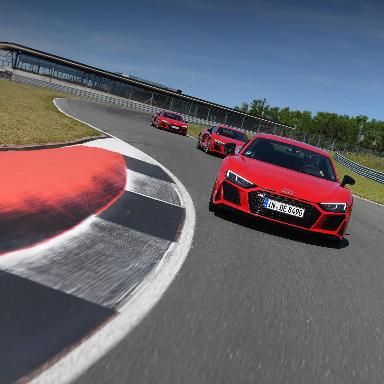 Drei rote Audi R8 Coupé V10 performance quattro fahren hintereinander auf einer Rennstrecke. Zur Audi sportscar experience.