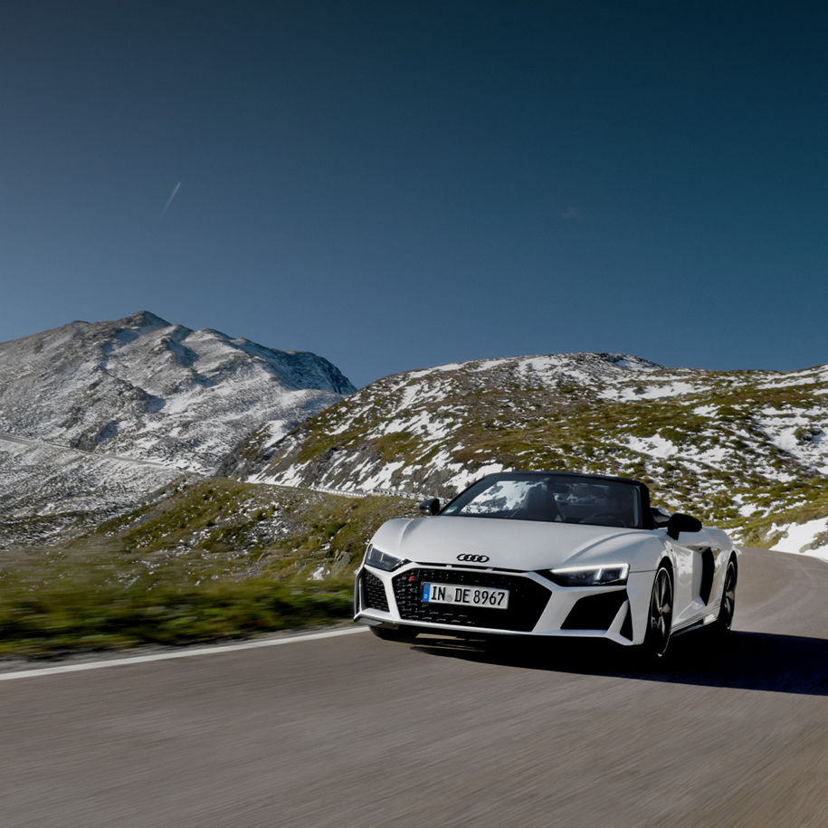 Audi R8 fährt einen Alpenpass entlang. Im Hintergrund sind mit Schnee bedeckte Berge zu sehen.