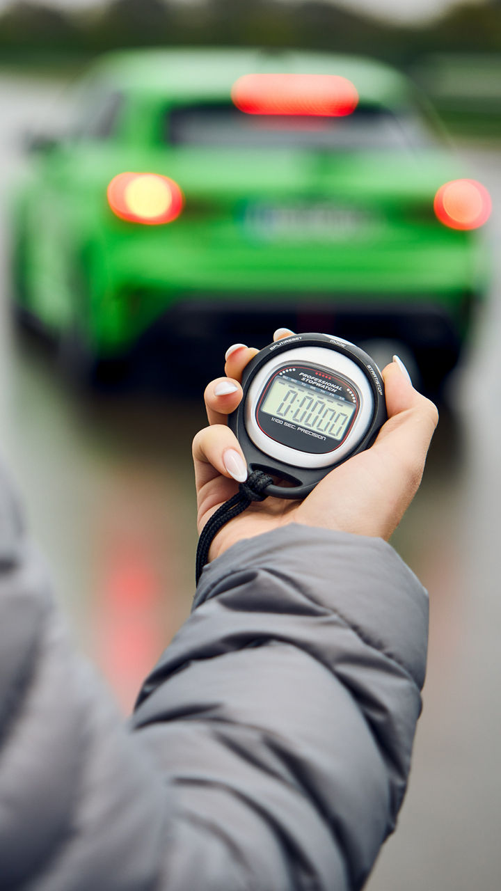 Jemand hält eine Stoppuhr in der Hand, im Hintergrund befindet sich ein hellgrünes Audi Modell