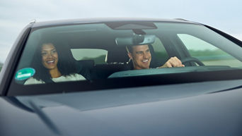 A man is sitting at the wheel of a grey Audi model. A woman is sitting next to him. They are both laughing.