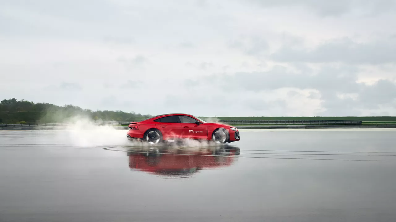 Roter Audi RS e-tron GT performance (Seitenansicht) fährt durch eine große Pfütze auf einem Übungsgelände 
