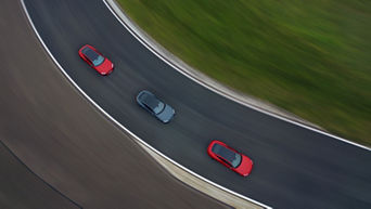 Draufsicht auf drei Audi Fahrzeuge, zwei rot und eines grau, auf einer Rennstrecke in einer Linkskurve.