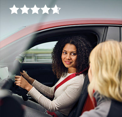 A woman is sitting at the wheel of an Audi model. An instructor leans towards her at the open car door and explains something to her.