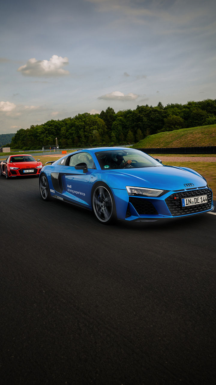 Blauer und roter Audi R8 Coupé fahren auf einer Rennstrecke hintereinander, der blaue Audi R8 fährt vorne