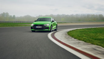 Light green Audi RS 3 Sportback driving around a bend on a training ground.