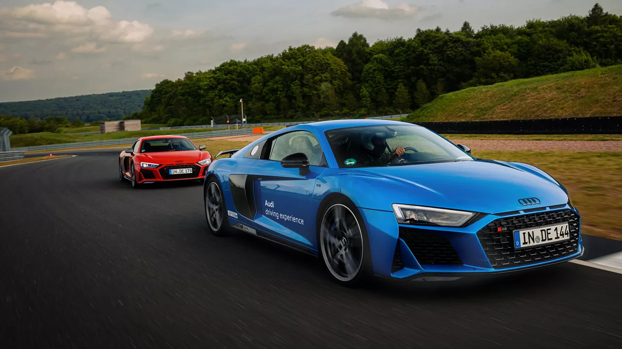 Blue and red Audi R8 Coupé drive behind each other on a race track, the blue Audi R8 drives in front 