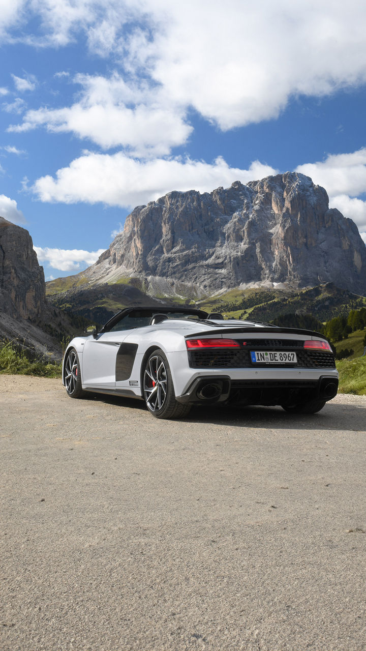 Weißer Audi R8 Spyder V10 performance quattro mit offenen Verdeck (Heckansicht) steht in den Bergen bei super Wetter