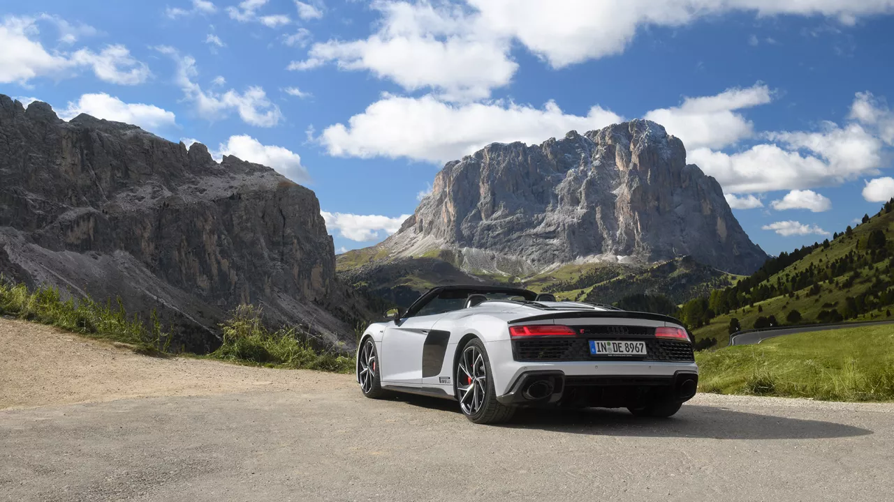 White Audi R8 Spyder V10 performance quattro with open top (rear view) standing in the mountains in great weather