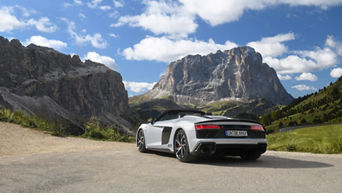 White Audi R8 Spyder V10 performance quattro with open top (rear view) standing in the mountains in sunny weather with few clouds.