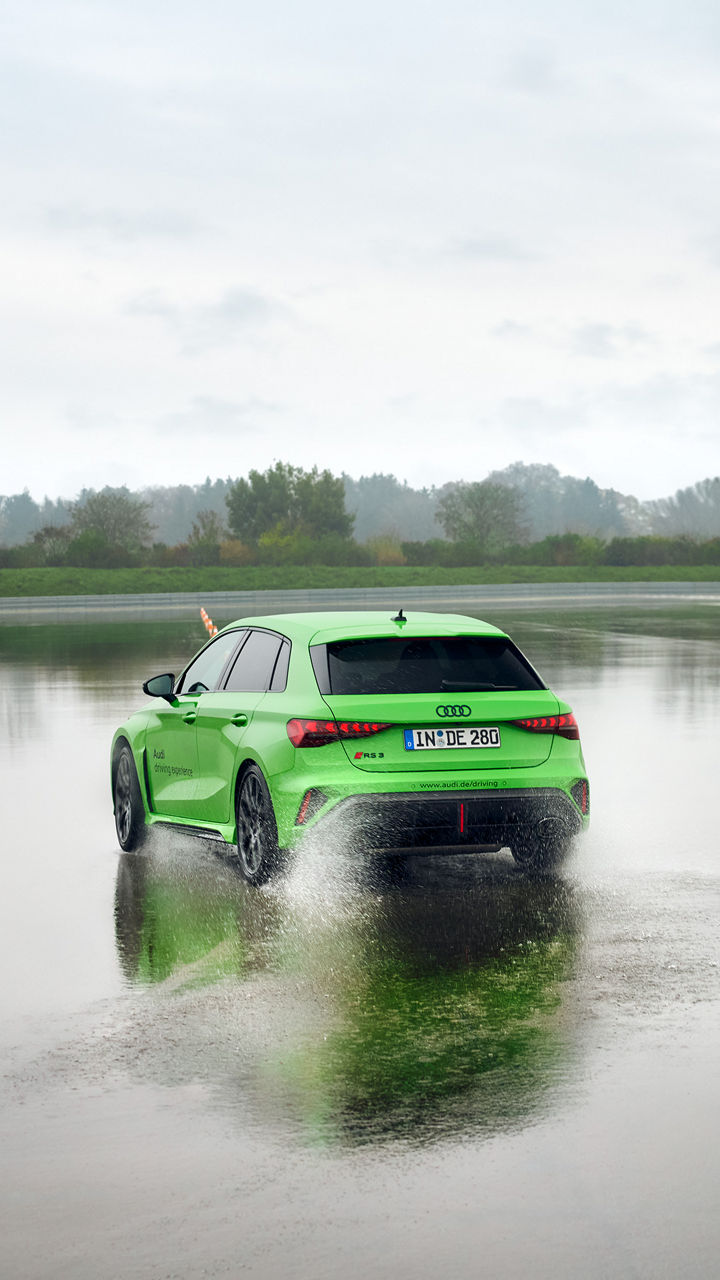 Hellgrüner Audi RS 3 Sportback fährt auf einem Übungsgelände über eine große Pfütze