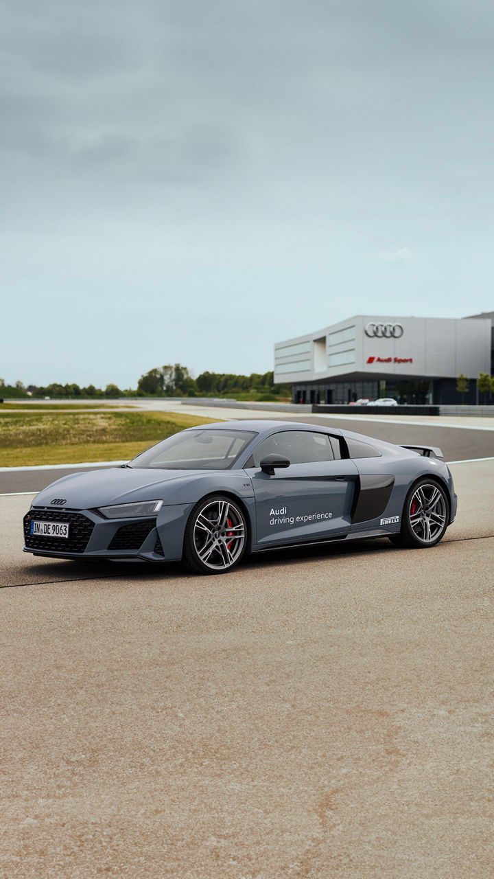 Mattgrauer Audi R8 Coupé fährt auf einer Strecke, im Hintergrund befindet sich ein Audi Sport Gebäude
