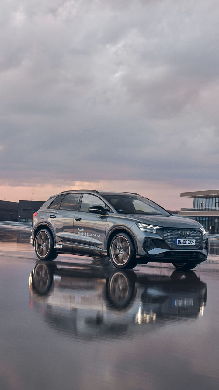Grauer Audi Q4 e-tron fährt auf einer nassen Fahrbahn bei einem Training
