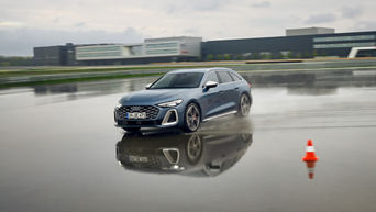 Audi S5 Avant fährt auf einem nassen Übungsgelände durch eine tiefe Pfütze, im Hintergrund befindet sich ein Audi Gebäude.