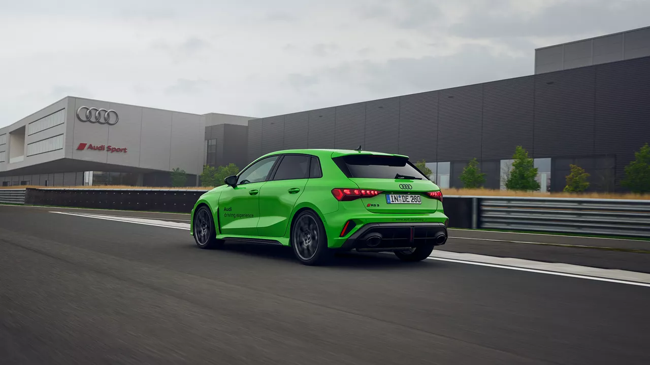 Light green Audi RS 3 Sportback on a training ground, in the background is a building with the Audi Sport logo