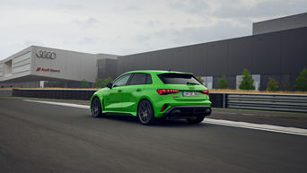 Hellgrüner Audi RS 3 Sportback auf einem Übungsgelände, im Hintergrund befindet sich ein Gebäude mit Audi Sport Logo.