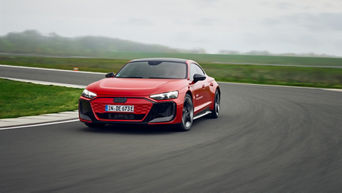 Roter Audi RS e-tron GT performance fährt auf einer Übungsstrecke durch eine Kurve, der Himmel ist bewölkt und grau.