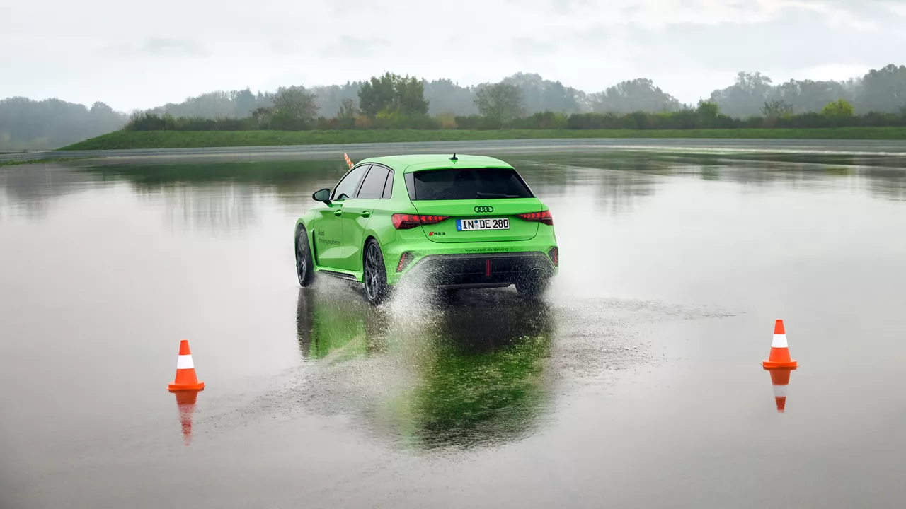 Light green Audi RS 3 Sportback drives over a large puddle on a training ground