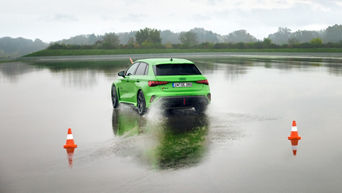 Hellgrüner Audi RS 3 Sportback fährt auf einem Übungsgelände über eine große Pfütze.
