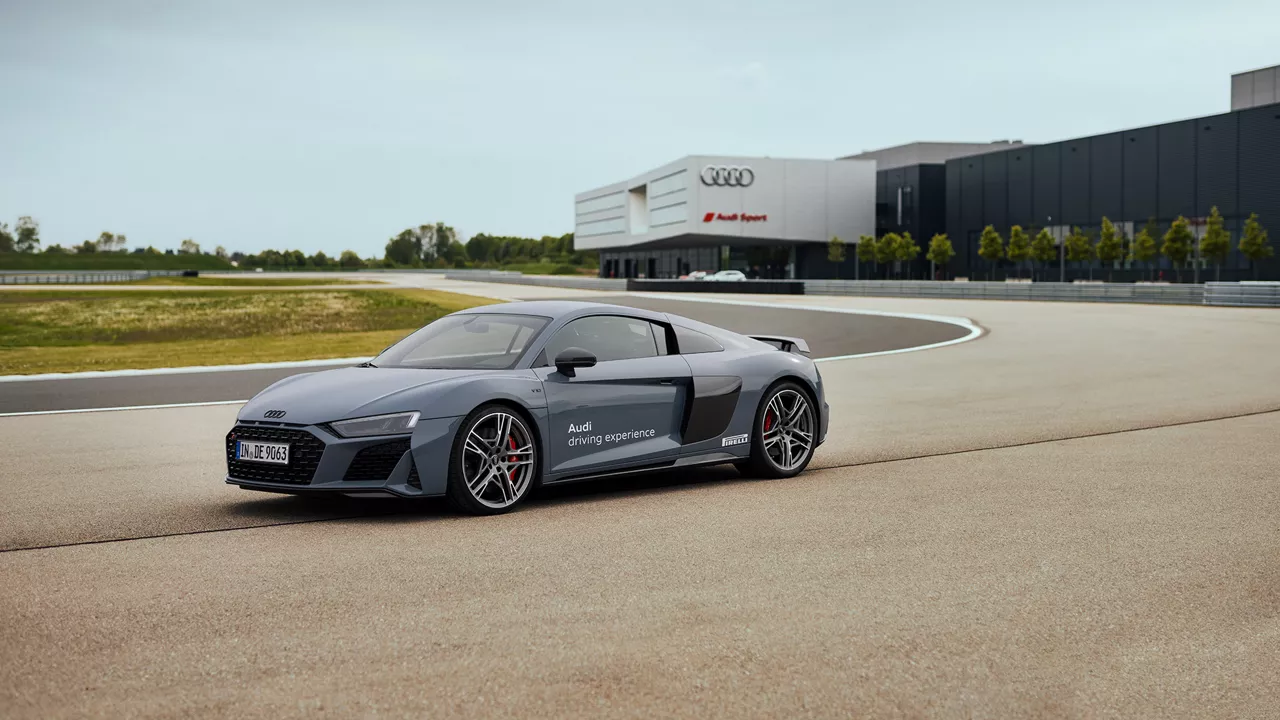 Matt gray Audi R8 Coupé driving on a track, with an Audi Sport building in the background