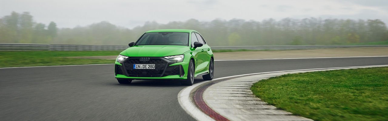 Light green Audi RS 3 Sportback drives on a bend in the road