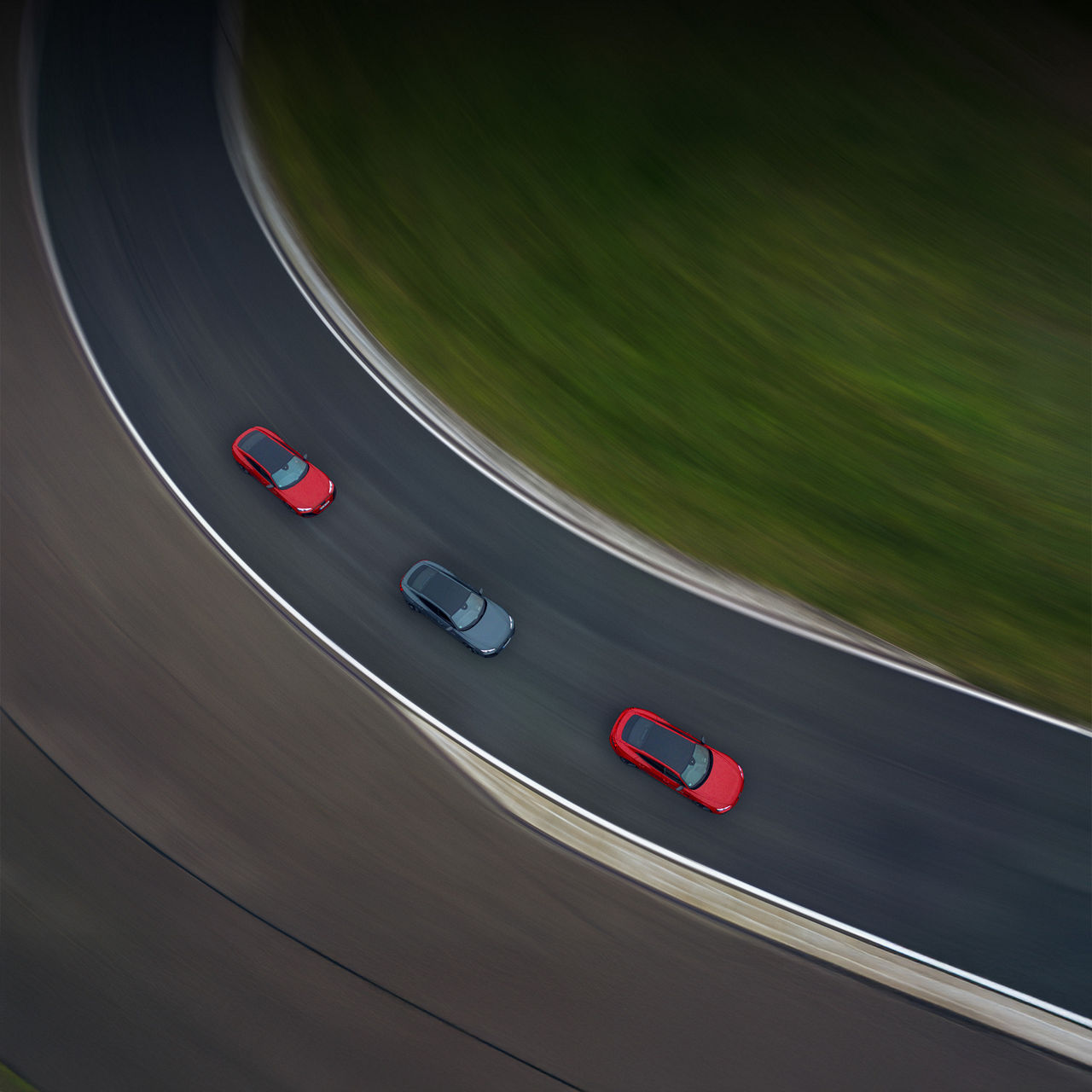 Drei Audi fahren nebeneinander durch eine langgezogene Kurve auf einer Teststrecke.