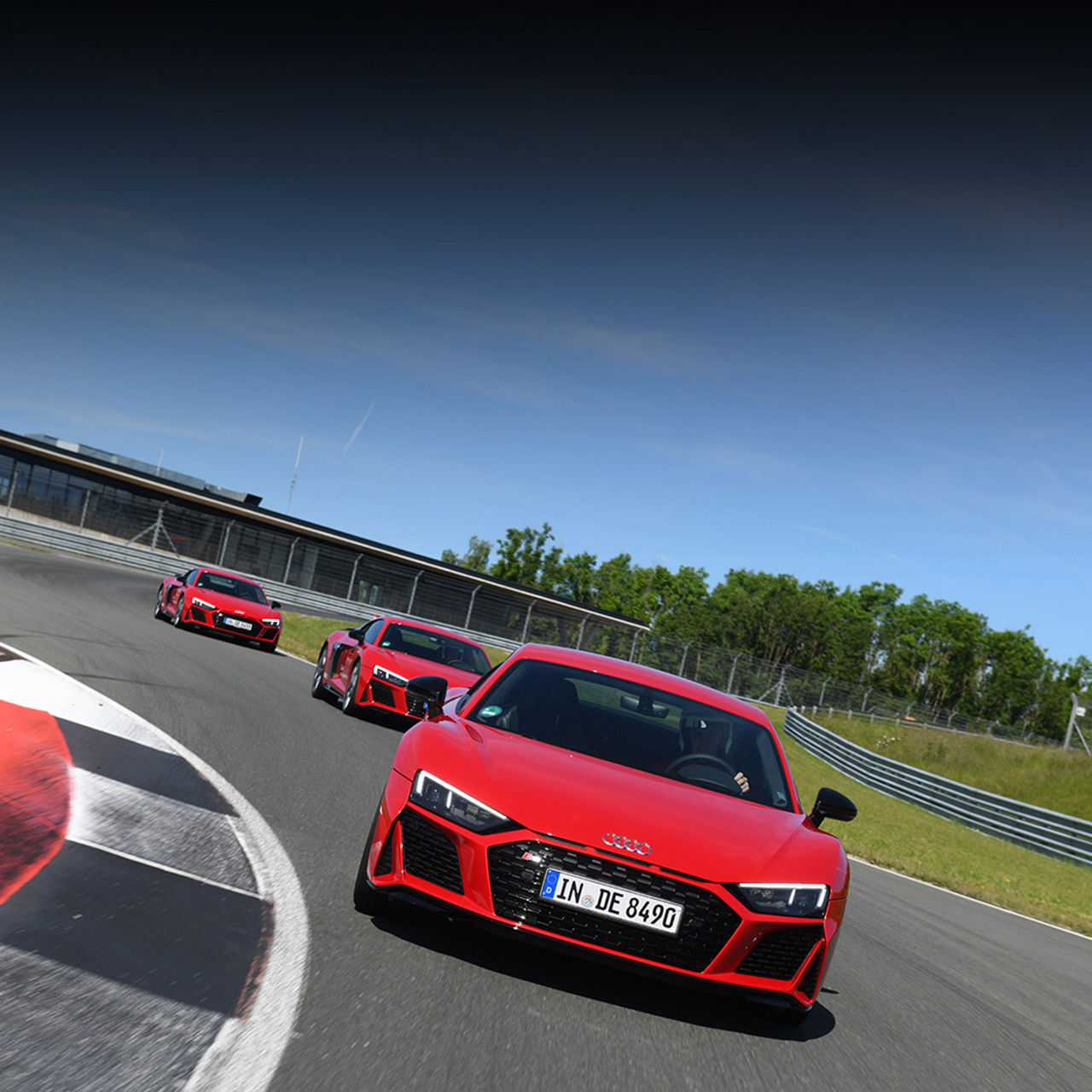 Drei rote Audi R8 Coupé fahren eng hintereinander auf einer Rennstrecke bei sonnigem Wetter.