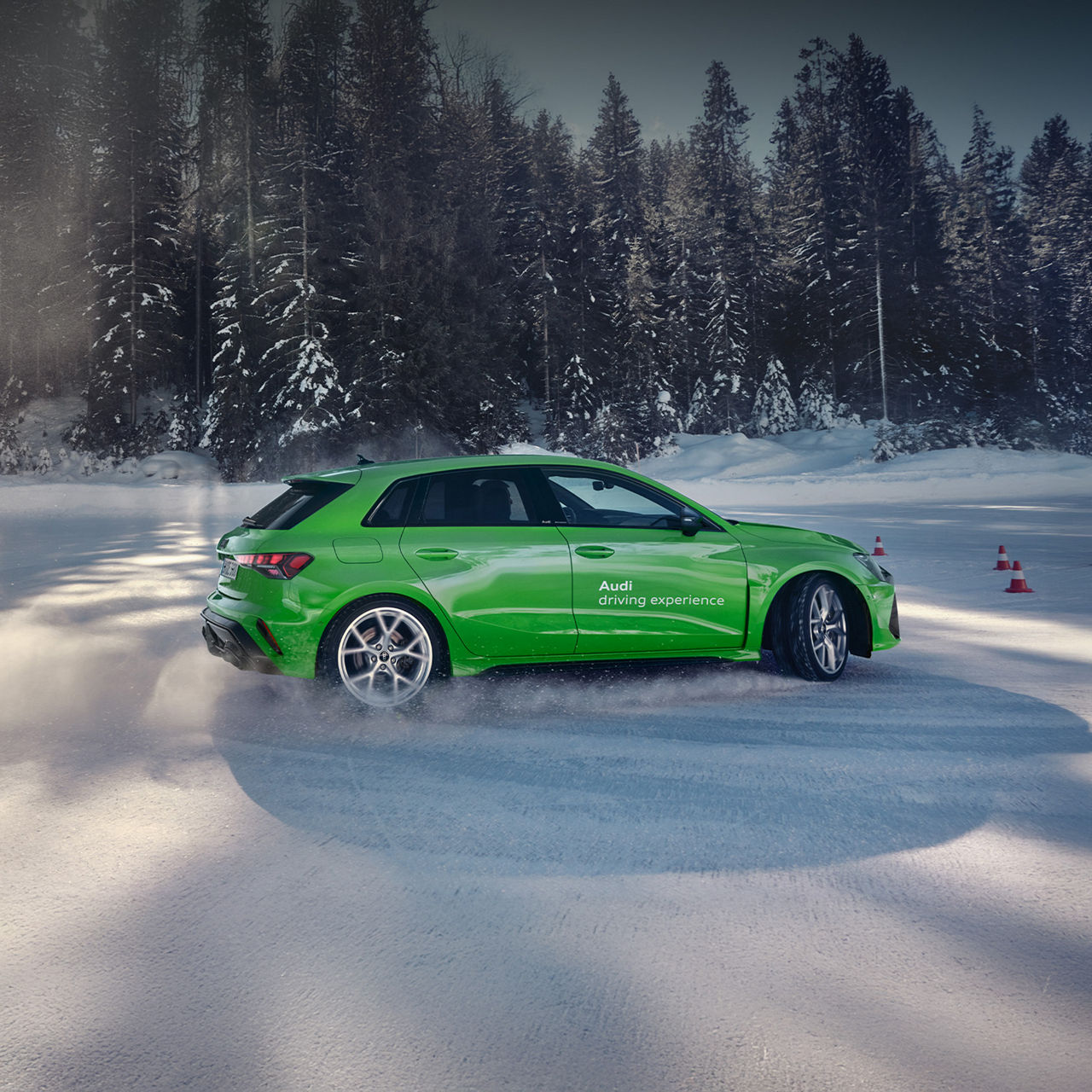 Hellgrüner Audi mit „driving experience“-Beschriftung driftet auf schneebedeckter Fläche im Wald.