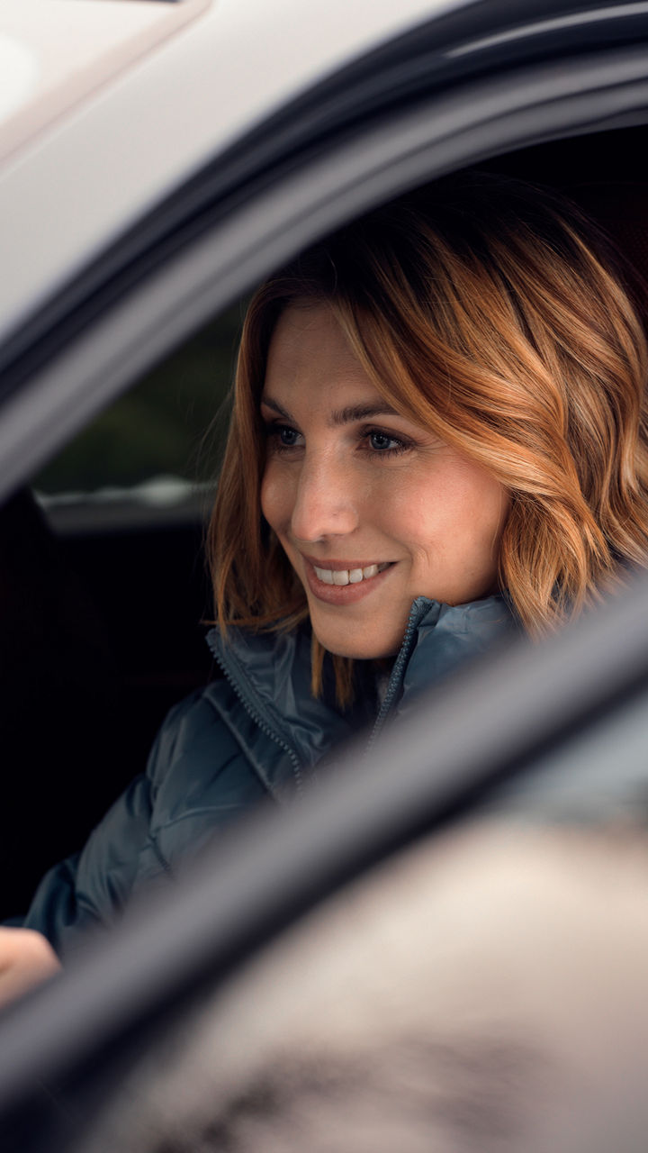 Woman with blond hair and blue jacket sits concentrated at the wheel of a vehicle.
