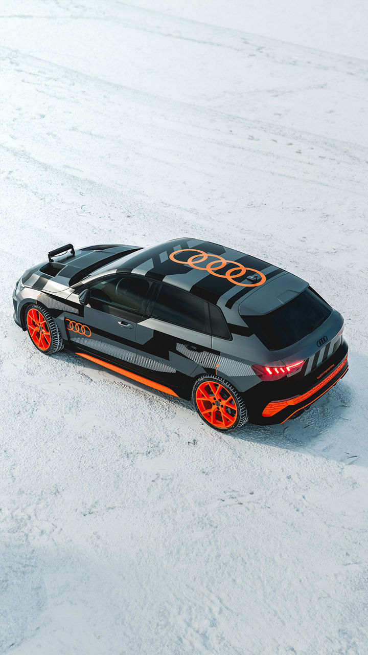 Schwarz-orange folierter Audi RS 3 driving experience mit auffälligem Felgendesign steht auf verschneitem Untergrund, fotografiert von schräg oben.