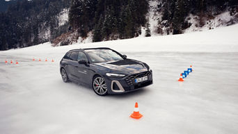 Dark Audi S5 Avant with “Audi driving experience” lettering on an icy track, surrounded by cones and a snowy forest backdrop.
