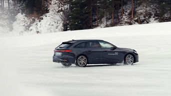 Dark Audi S5 Avant with white “Audi driving experience” lettering drifts over a snow-covered surface.