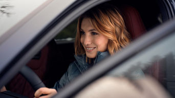 Woman with blond hair and blue jacket sits concentrated at the wheel of a vehicle.
