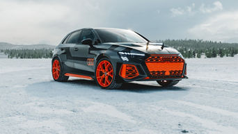 Black Audi RS 3 driving experience with eye-catching orange and red rims and details stands on a snow-covered surface against a wooded background.