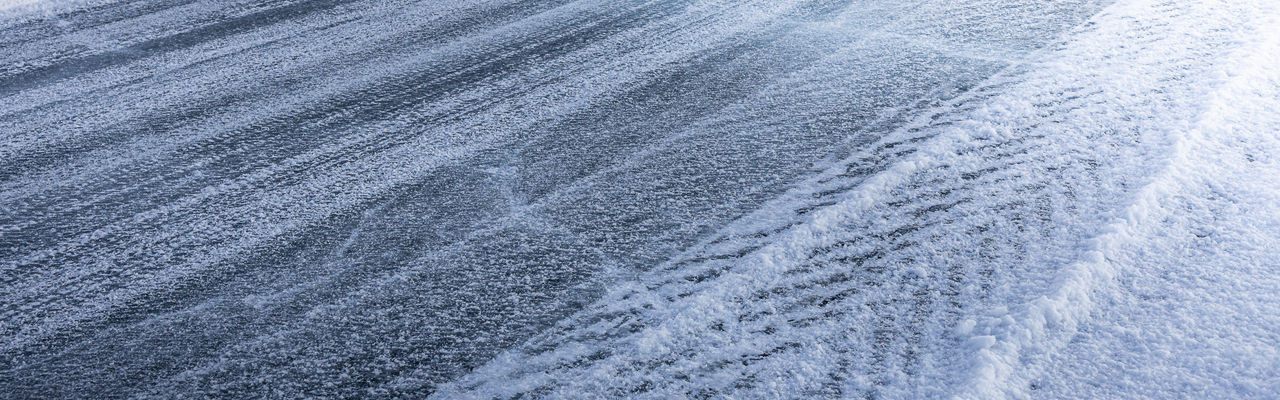 Textured, icy road with tire tracks and snow on the side.
