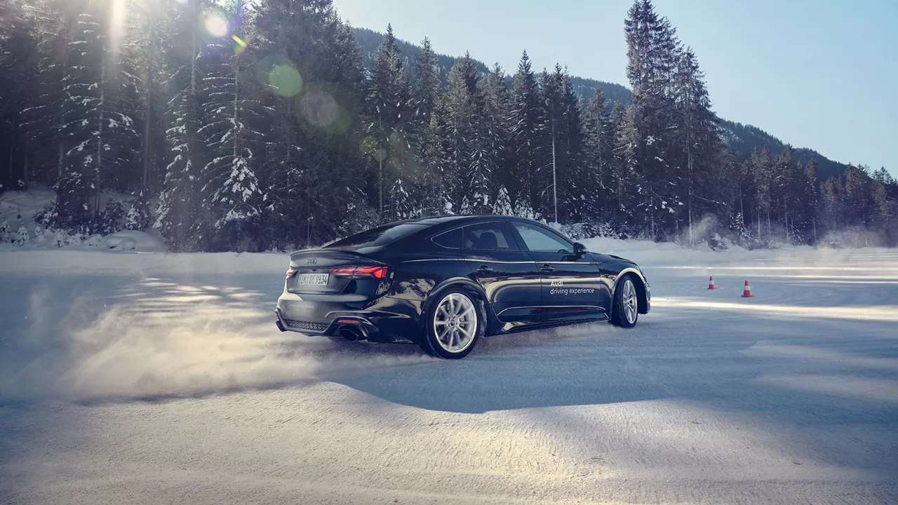 Schwarzer Audi RS 5 Sportback von der Seite im Schnee, im Hintergrund Wälder und Sonnenschein