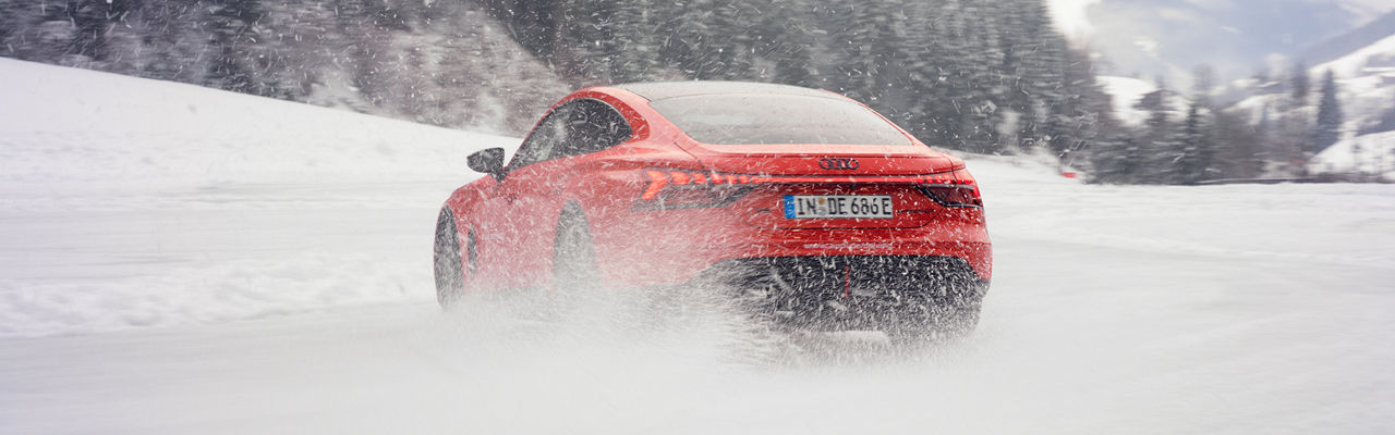 Roter Audi RS e-tron GT performance fährt auf schneebedeckter Strecke, aufgewirbelter Schnee verdeckt teilweise das Fahrzeugheck.