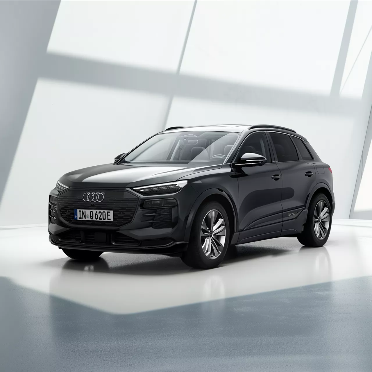 Weißer Audi Q6 e-tron steht am Sandstrand mit Blick auf das Meer und eine felsige Küstenlandschaft im Hintergrund.