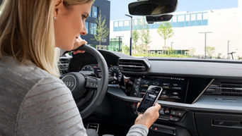 Frau sitzt im Auto und schaut auf ihr Handy