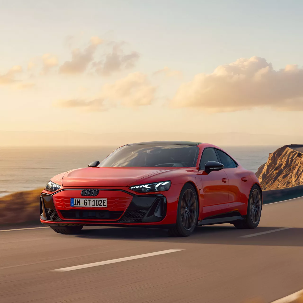 Ein roter e-tron GT quattro fährt auf einer Landstraße entlang einer Küste.