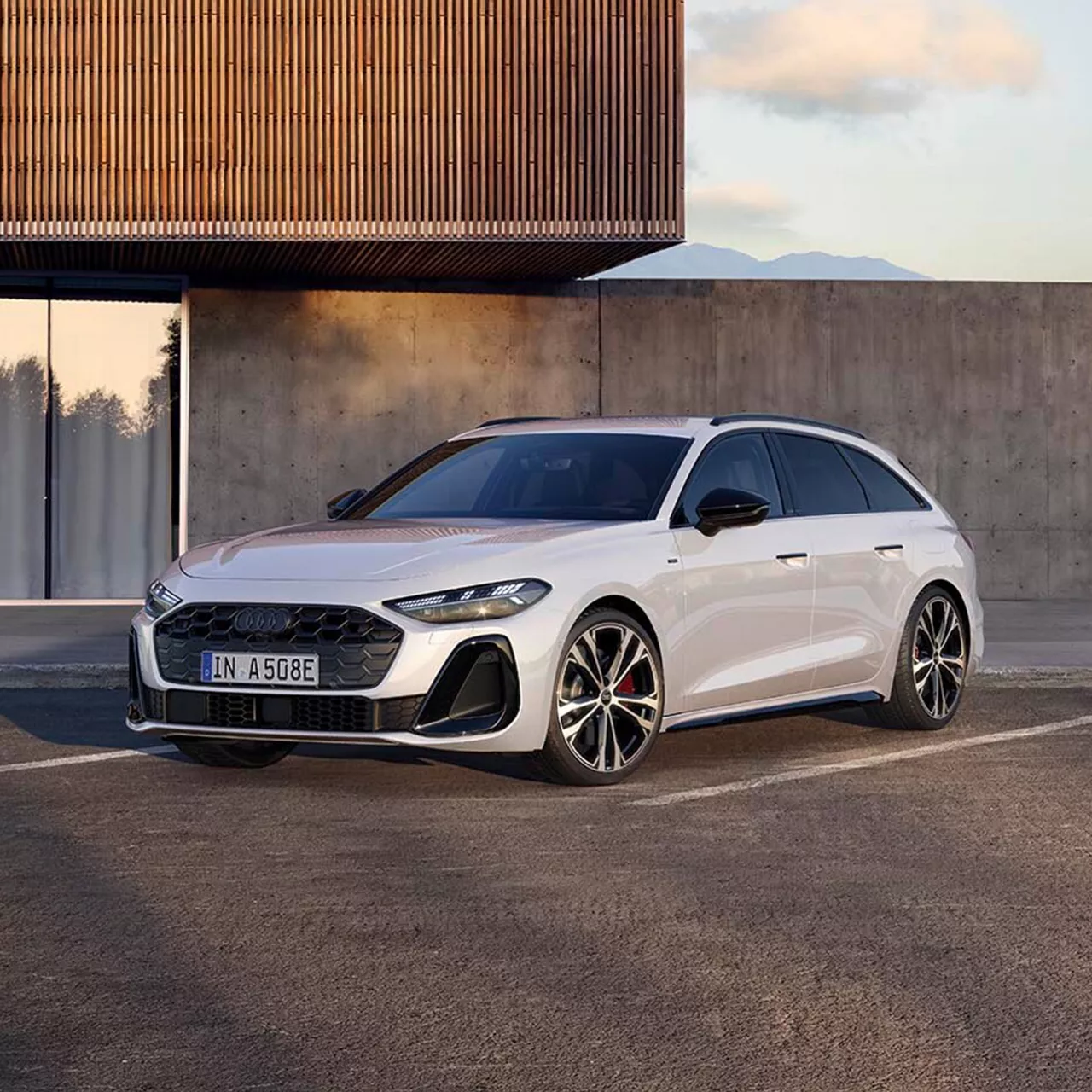 Ein weißer A5 Avant 220 kw e-hybrid steht seitlich vor einem beigen Gebäude