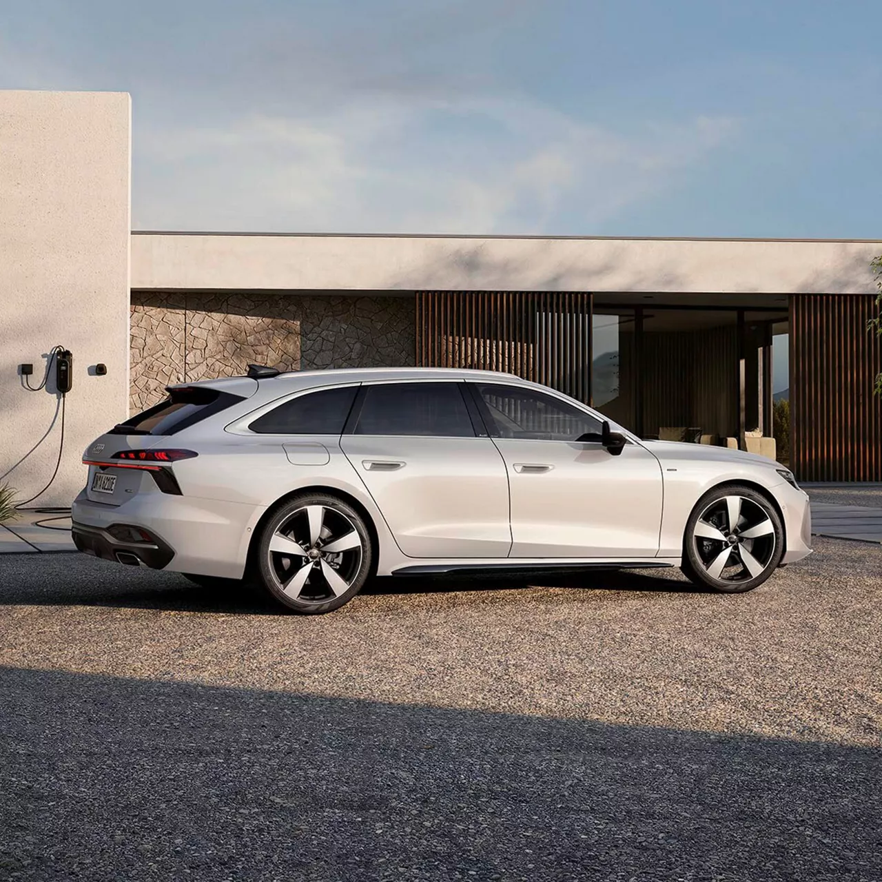 Weißer A6 Avant e-hybrid steht seitlich von hinten vor einer Ladestation