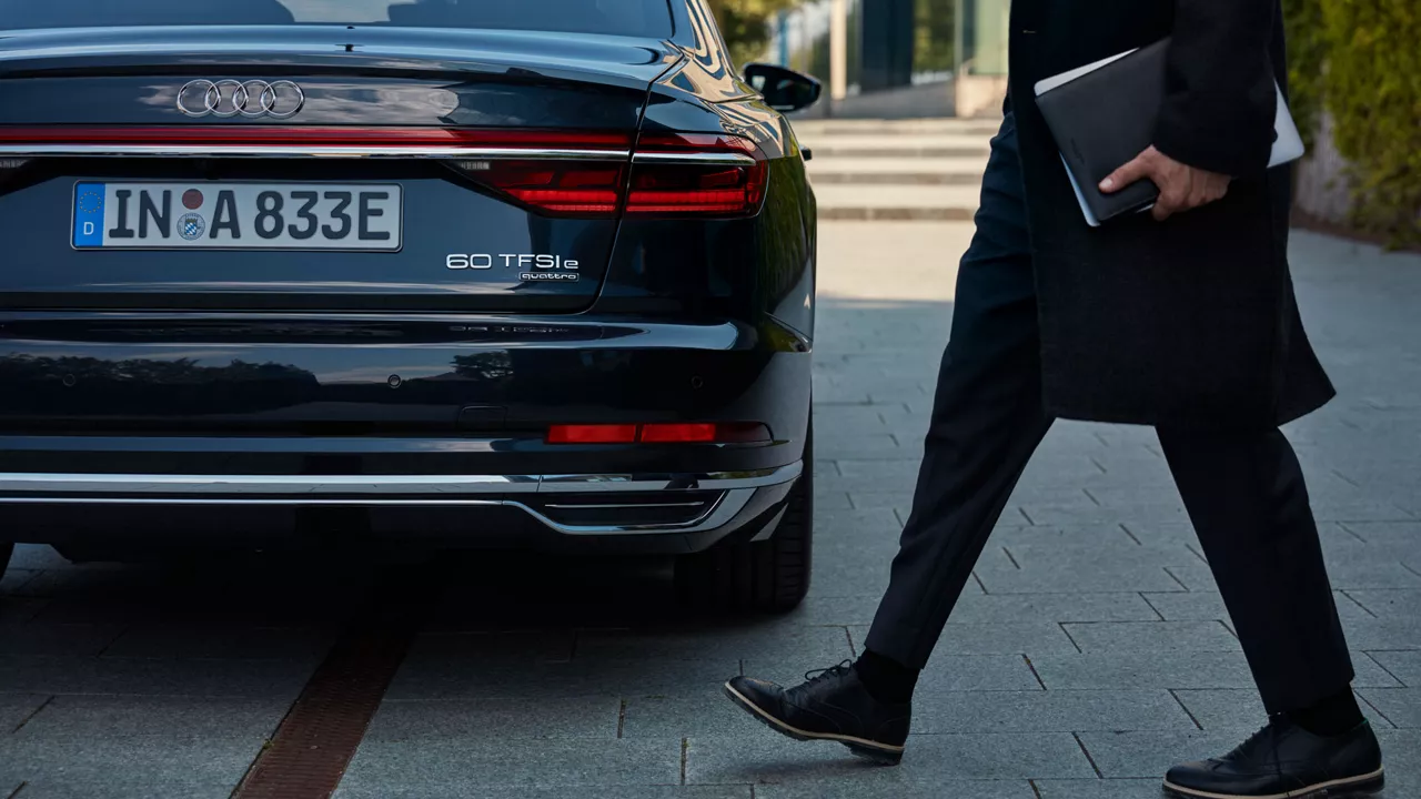 Ein Mann läuft an einem Audi vorbei, mit Akten unter dem Arm