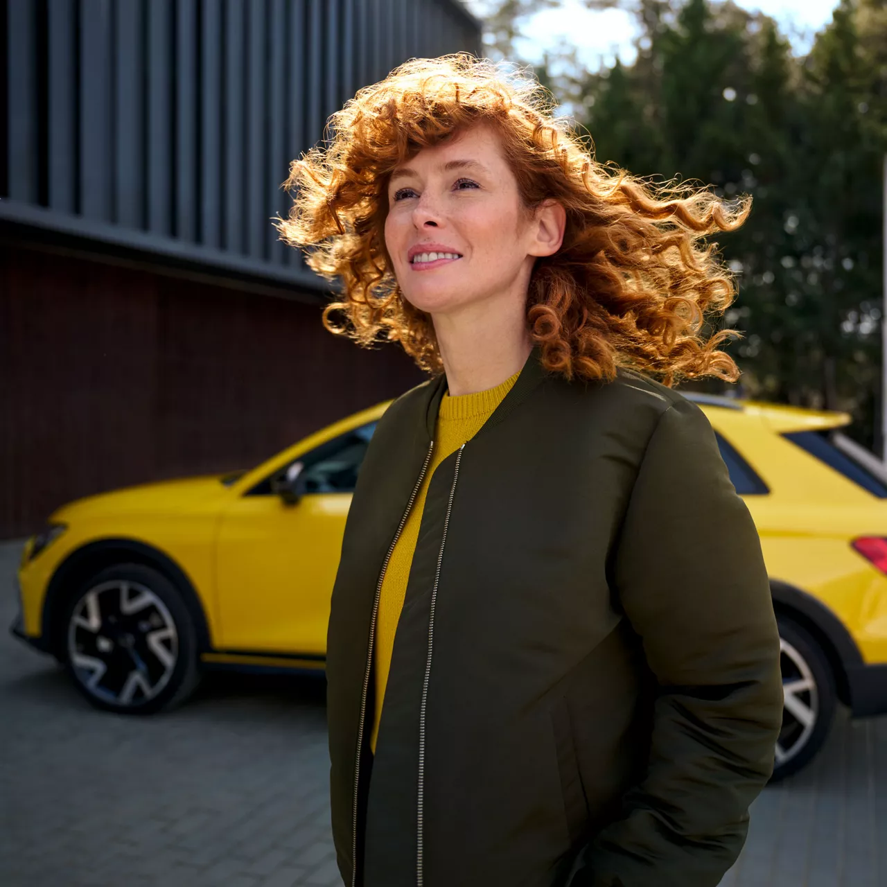 Eine rothaarige Frau steht vor einem gelben Audi