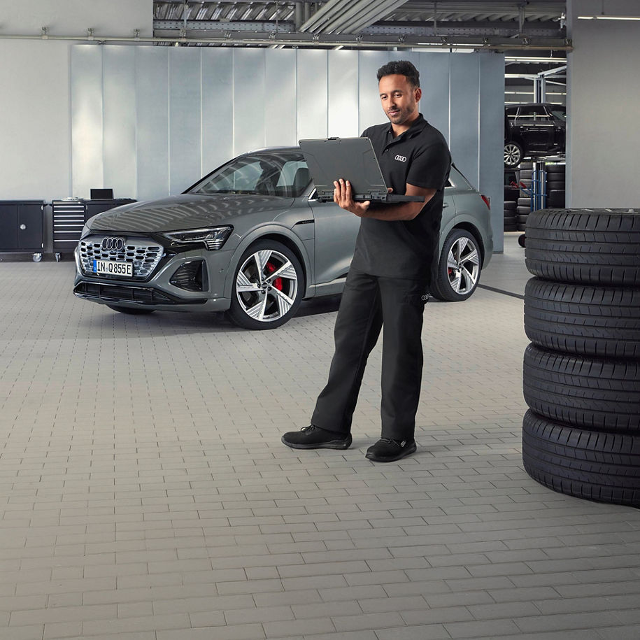Ein Mann steht mit einem Laptop in der Hand in einer Werkstatt vor einem silbernen Audi