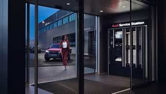 Eine Audi Service Station steht in einem Gebäude und ein roter Audi mit einer Frau steht draußen vor der Tür