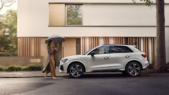 Eine Frau läuft mit einem Regenschirm vor einem weißen Audi