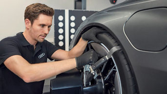 Mann trägt Handschuhe und hat seine Hände auf einem Audi Reifen, der sich an einem Audi befindet